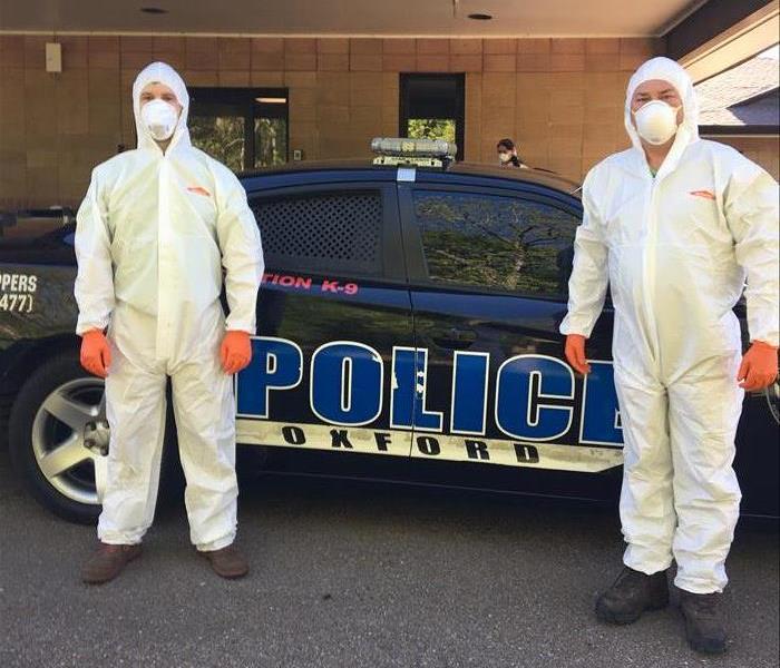 Two men in PPE standing in front of Oxford Police Car