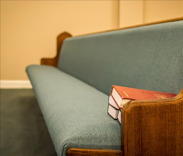 A Bible sits on an empty church pew on a carpeted floor.