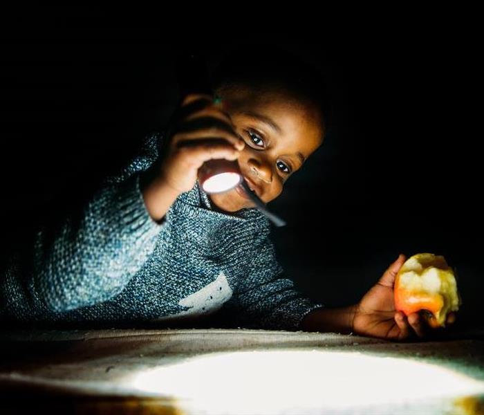A young boy reads a book by flashlight while holding an apple